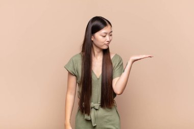 Asyalı genç bir kadın kendini mutlu hissediyor ve gülümsüyor. Yan taraftaki bir nesneye ya da konsepte bakıyor.