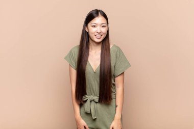 Asyalı genç bir kadın neşeli bir şekilde gülümsüyor. Olumlu, mutlu, kendinden emin ve rahat bir ifadeyle.