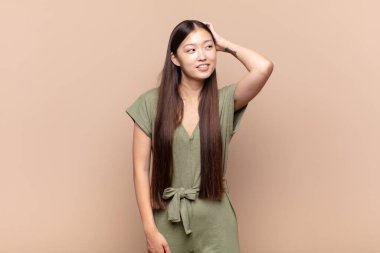 Asyalı genç bir kadın neşeli ve sıradan bir şekilde gülümsüyor, olumlu, mutlu ve kendinden emin bir bakışla göğüs göğüse tutuşuyor.