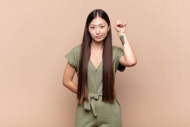 Asyalı genç kadın kendini ciddi, güçlü ve asi hissediyor, yumruğunu kaldırıyor, protesto ediyor ya da devrim için savaşıyor.