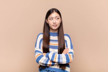 Asyalı genç bir kadın kuşkulanıyor ya da düşünüyor, dudağını ısırıyor ve kendini güvensiz ve gergin hissediyor.