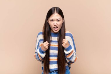 Asyalı genç bir kadın sinirli, sinirli, sinirli bakışlar ve sıkı yumruklarla bağırıyor. Öfkeli hissediyor.