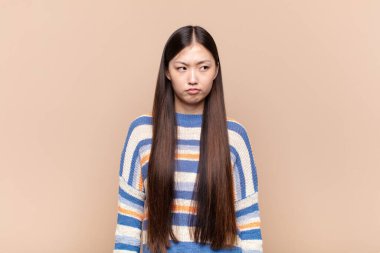 Asyalı genç bir kadın üzgün, üzgün ya da kızgın. Olumsuz bir tavır sergiliyor, anlaşmazlık içinde kaşlarını çatıyor.