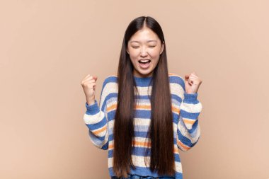 Asyalı genç kadın son derece mutlu ve şaşırmış görünüyor, başarıyı kutluyor, bağırıyor ve zıplıyor.