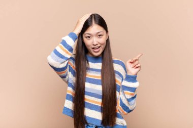 Asyalı genç kadın gülüyor, mutlu, pozitif ve şaşırmış görünüyor, yanal fotokopi alanını işaret eden harika bir fikrin farkına varıyor.