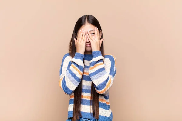 アジア系の若い女性が手で顔を覆い驚くような表情で指の間を見て — ストック写真