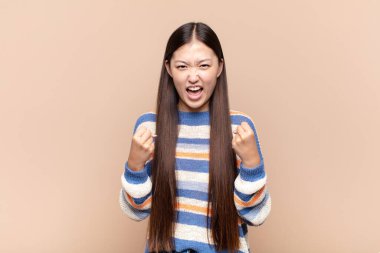 Asyalı genç kadın zaferle bağırıyor, gülüyor, mutlu ve heyecanlı hissediyor ve başarıyı kutluyor.