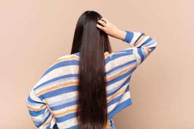 Asyalı genç bir kadın bilgisiz ve kafası karışık hissediyor, bir çözüm düşünüyor, eli kalçasında, diğeri kafasında, dikiz aynasından.