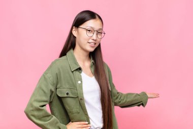 Asyalı genç bayan kendini mutlu ve neşeli hissediyor, gülümsüyor ve sizi hoş karşılıyor, sizi dostça bir jestle içeri davet ediyor.