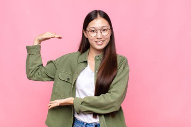 Asyalı genç kadın gülümsüyor, mutlu, pozitif ve tatmin olmuş hissediyor, fotokopi alanında nesne ya da konsept tutuyor ya da gösteriyor