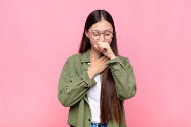 Asyalı genç bir kadın boğazı ağrıyan ve grip belirtileri gösteren ağzı kapalı öksüren bir hasta.