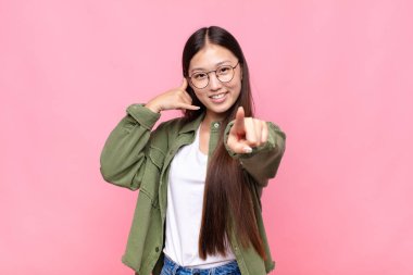 Asyalı genç bir kadın neşeyle gülümsüyor ve kamerayı işaret ederek seni daha sonra arıyor, telefonla konuşuyor.