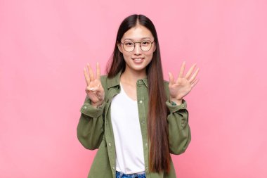 Asyalı genç bir kadın gülümsüyor ve arkadaş canlısı görünüyor, 8 ya da 8 numarayı gösteriyor, eli önde, geri sayıyor.