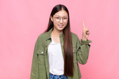 Asyalı genç kadın mutlu bir şekilde gülümsüyor, tek eliyle uzayı işaret ediyor.