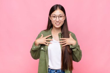 Asyalı genç kadın mutlu, şaşırmış, gururlu ve heyecanlı görünüyor.