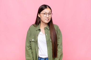 Asyalı genç bir kadın şaşkın ve şaşkın görünüyor. Sinirli bir hareketle dudağını ısırıyor. Sorunun cevabını bilmiyor.