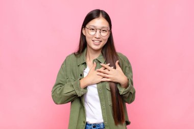 Asyalı genç bir kadın romantik, mutlu ve aşık, neşeyle gülümsüyor ve kalbe yakın el ele tutuşuyor.