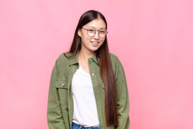 Asyalı genç bir kadın neşeli bir şekilde gülümsüyor. Olumlu, mutlu, kendinden emin ve rahat bir ifadeyle.