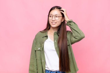 Asyalı genç bir kadın neşeli ve sıradan bir şekilde gülümsüyor, olumlu, mutlu ve kendinden emin bir bakışla göğüs göğüse tutuşuyor.