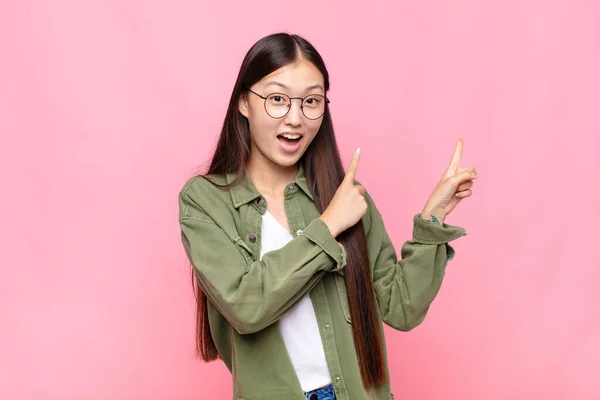 アジア系の若い女性は喜びと驚きの表情で笑顔で横を指差しています — ストック写真