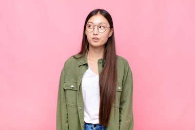 Asyalı genç kadın şaşkın, mutlu, şaşkın ve şaşırmış hissediyor, ağzı açık bir şekilde yana bakıyor.