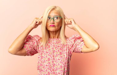 Orta yaşlı bir kadın kafası karışık ya da şüpheci, bir fikre odaklanmış, çok düşünüyor, kenarda boşluklar arıyor.