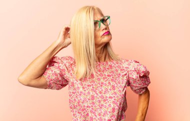 Orta yaşlı kadın şaşkın ve şaşkın hissediyor, kafasını kaşıyor ve yan tarafa bakıyor.