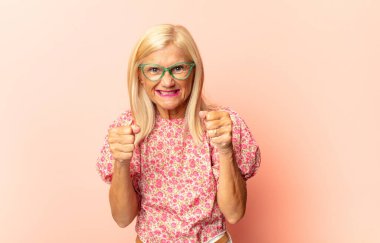 Orta yaşlı bir kadın sinirli, sinirli, kızgın bakışlar ve sıkı yumruklarla bağırıyor. Öfkeli hissediyor.