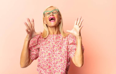 Orta yaşlı bir kadın kameraya iki parmağını ve kızgın bir ifadeyle bakarak sana görevini yapmanı söylüyor.