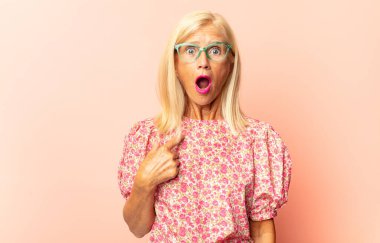 Orta yaşlı bir kadın korkmuş ya da utanmış hisseder. Gözleri yarı kapalı, yarı çıplak bir şekilde dikizler ya da gözetler.