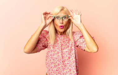 Orta yaşlı kadın şaşkın ve şaşırmış hissediyor. Kenardaki fotokopi alanını işaret ediyor. Şaşırmış ve ağzı açık bakıyor.