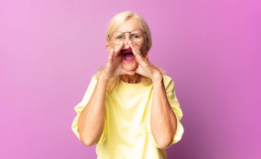Orta yaşlı kadın mutlu, heyecanlı ve pozitif hissediyor. Elleri ağızda, bağırarak bağırıyor.