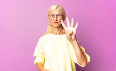 Orta yaşlı bir kadın gülümsüyor ve arkadaş canlısı görünüyor. Elleri önde, geriye doğru sayıyor.