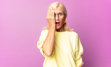 Orta yaşlı bir kadın uykulu, sıkılmış ve esniyor, baş ağrısı ve yüzünün yarısını kaplayan bir elle.