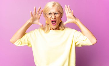 Orta yaşlı bir kadın elleri havada bağırıyor. Öfkeli, sinirli, stresli ve üzgün.