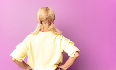 Orta yaşlı bir kadın kafası karışık ya da dolgun ya da şüphe ve soru dolu, merak ediyor, elleri kalçasında, dikiz aynasından.