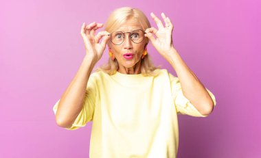 Orta yaşlı kadın şaşkın, şaşırmış ve şaşırmış hissediyor, elinde şaşkın, inançsız bir bakışla gözlük tutuyor.
