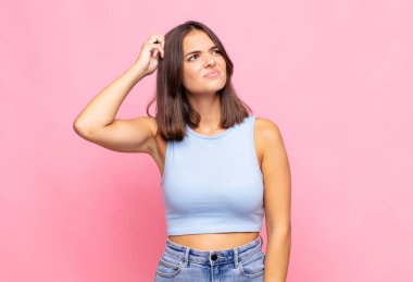 Genç, güzel bir kadın şaşkın ve kafası karışmış hissediyor, başını kaşıyor ve yan tarafa bakıyor.