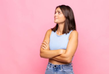 Genç, güzel bir kadın omuz silkiyor, kafası karışık ve kararsız, kolları bağlı ve şaşkın görünüyor.