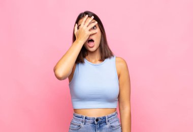 Genç, güzel bir kadın şok olmuş, korkmuş ya da korkmuş görünüyor. Yüzü elle kaplanmış ve parmaklarının arasından gizlice bakıyor.