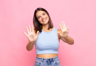 Genç, güzel bir kadın gülümsüyor ve dost canlısı görünüyor. 9 ya da 9 numarayı gösteriyor.