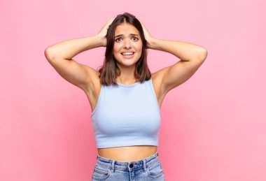 Genç, güzel bir kadın kendini stresli, endişeli, endişeli ya da korkmuş hissediyor. Elleri başının üstünde, hatayla panikliyor.