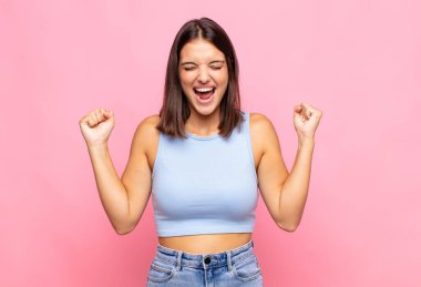 Genç ve güzel bir kadın son derece mutlu ve şaşırmış görünüyor, başarıyı kutluyor, bağırıyor ve zıplıyor.