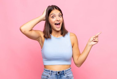 Genç, güzel bir kadın gülüyor, mutlu, pozitif ve şaşırmış görünüyor, yanal fotokopi alanını işaret eden harika bir fikri fark ediyor.