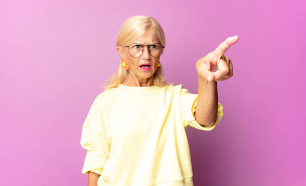 Женщина средних лет в шоке и удивлении, указывая и с изумлением глядя вверх, с открытым ртом смотрит