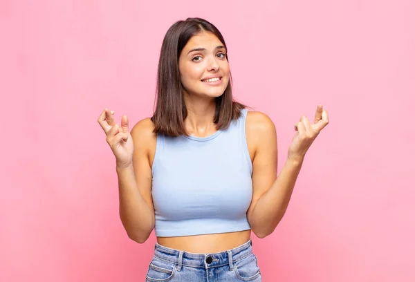 young pretty woman crossing fingers anxiously and hoping for good luck with a worried look