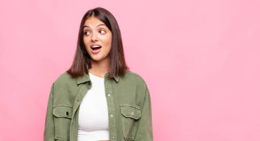 Genç, güzel bir kadın şaşkın, mutlu, şaşkın ve şaşırmış hissediyor, ağzı açık bir şekilde yana bakıyor.