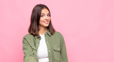 Genç, güzel bir kadın gülümsüyor, mutlu, kendinden emin ve arkadaş canlısı görünüyor, bir anlaşmaya varmak için el sıkışmayı teklif ediyor, işbirliği yapıyor.