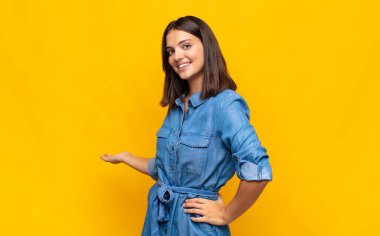 Genç ve güzel bir kadın mutlu ve neşeli hissediyor, gülümsüyor ve seni selamlıyor, dostça bir jestle içeri davet ediyor.