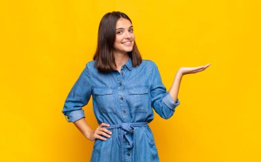 Genç, güzel bir kadın gülümsüyor, kendinden emin, başarılı ve mutlu hissediyor, fotokopi alanında fikir veya konsept gösteriyor.